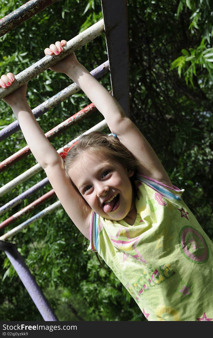 The little girl hangs on a crossbeam, has a good time in park of entertainments. The little girl hangs on a crossbeam, has a good time in park of entertainments