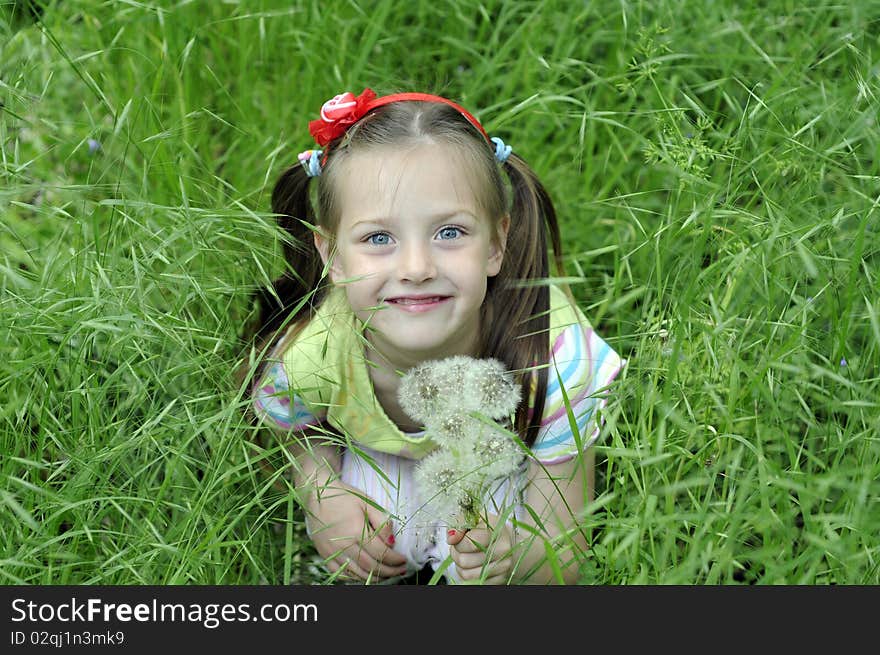 The little girl with dandelions in hands, sits in a green grass. The little girl with dandelions in hands, sits in a green grass