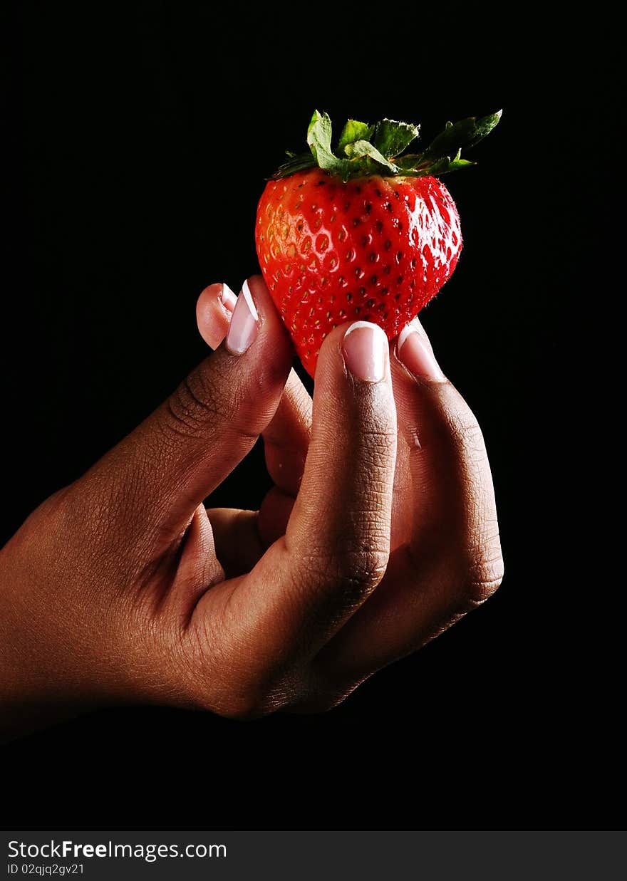 Womand holding a strawberry on a black backdround