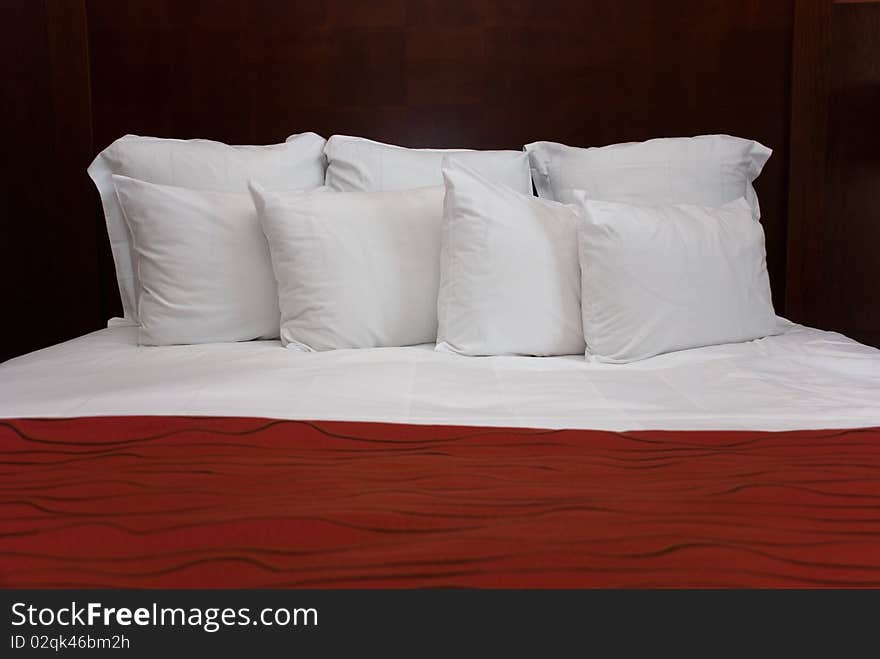 Eight white fluffy pillows on white sheets with a red bedspread against a wood headboard. Eight white fluffy pillows on white sheets with a red bedspread against a wood headboard.