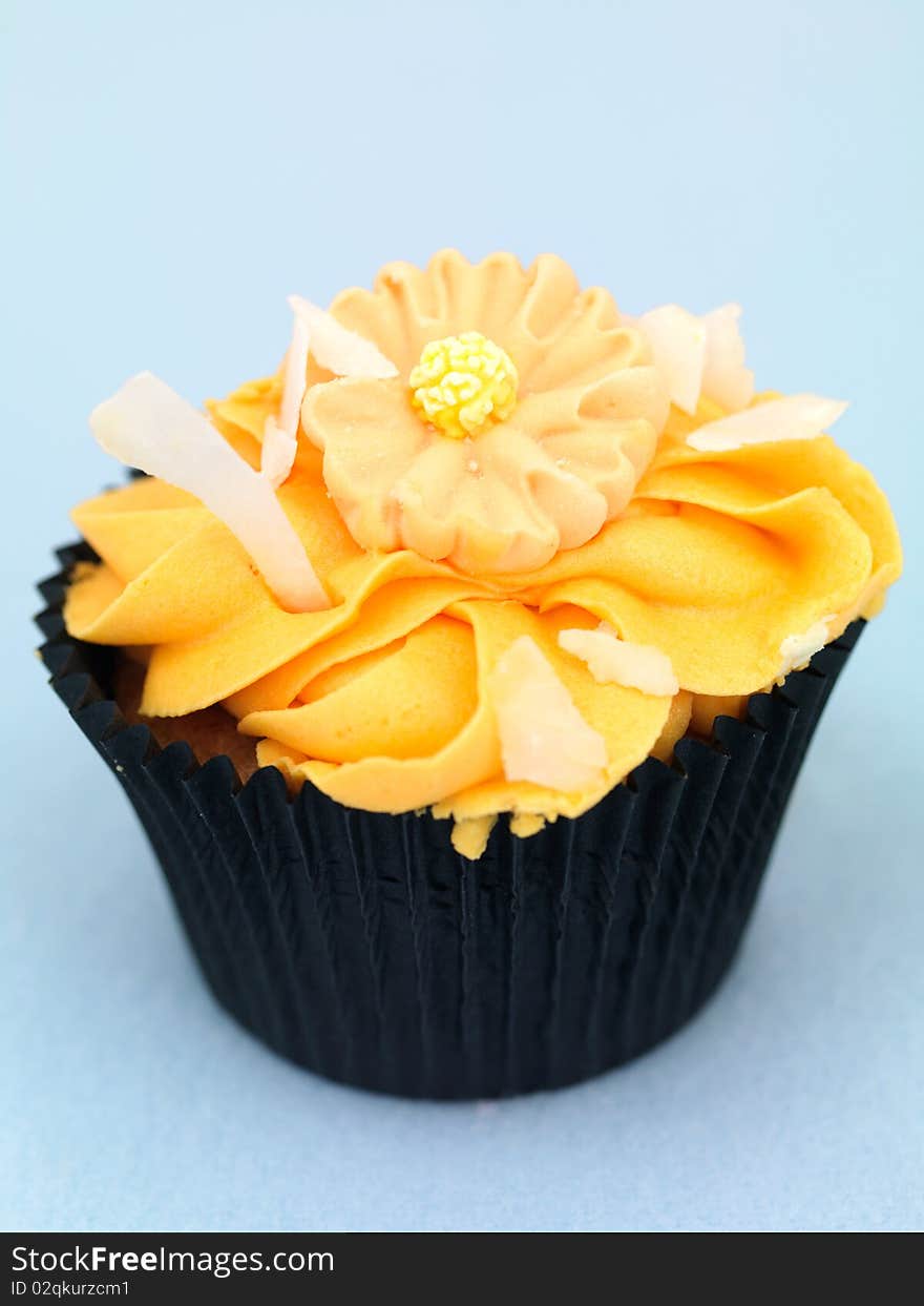 A freshly baked cup cake with orange frosting