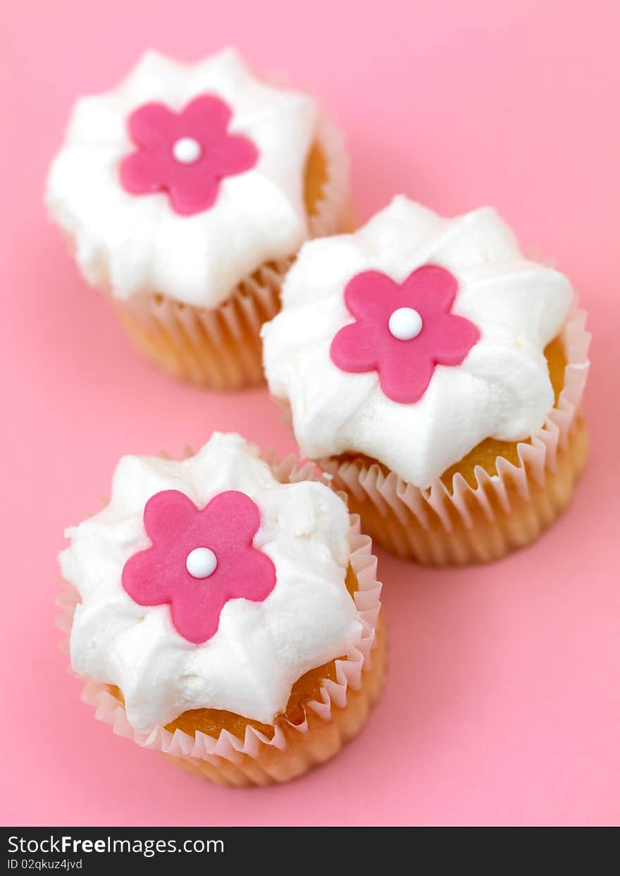 Freshly baked cup cakes with pink flowers and white frosting