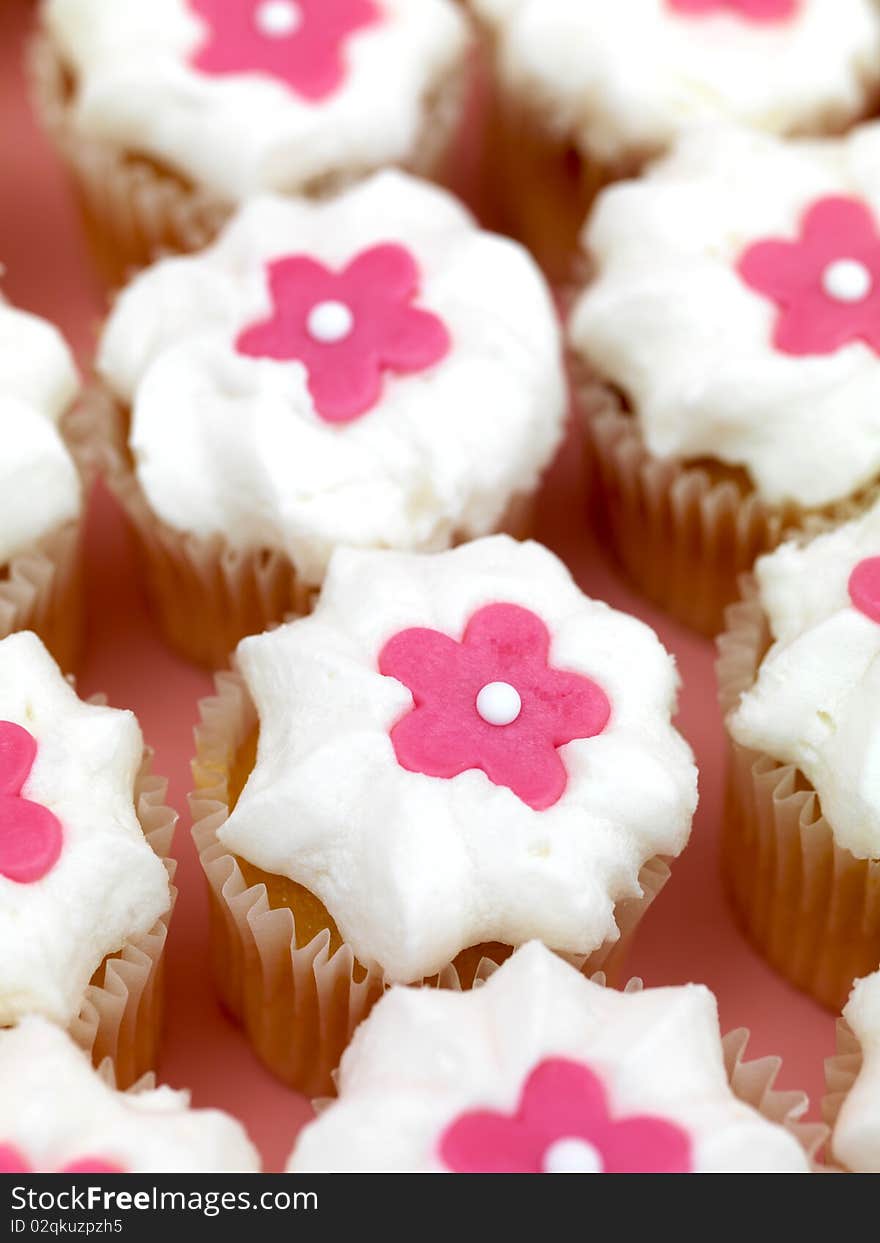 Freshly baked cup cakes with pink flowers and white frosting