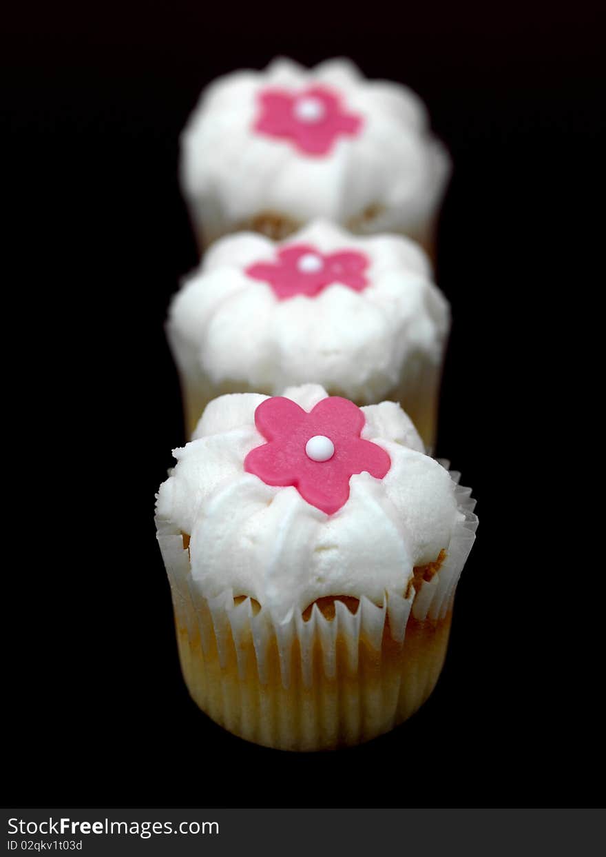 Freshly baked cup cakes with pink flowers and white frosting