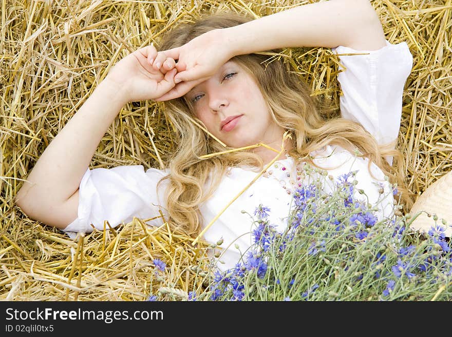 Woman lays on straw with a bunch of flowers in the summer and only has woken up. Woman lays on straw with a bunch of flowers in the summer and only has woken up