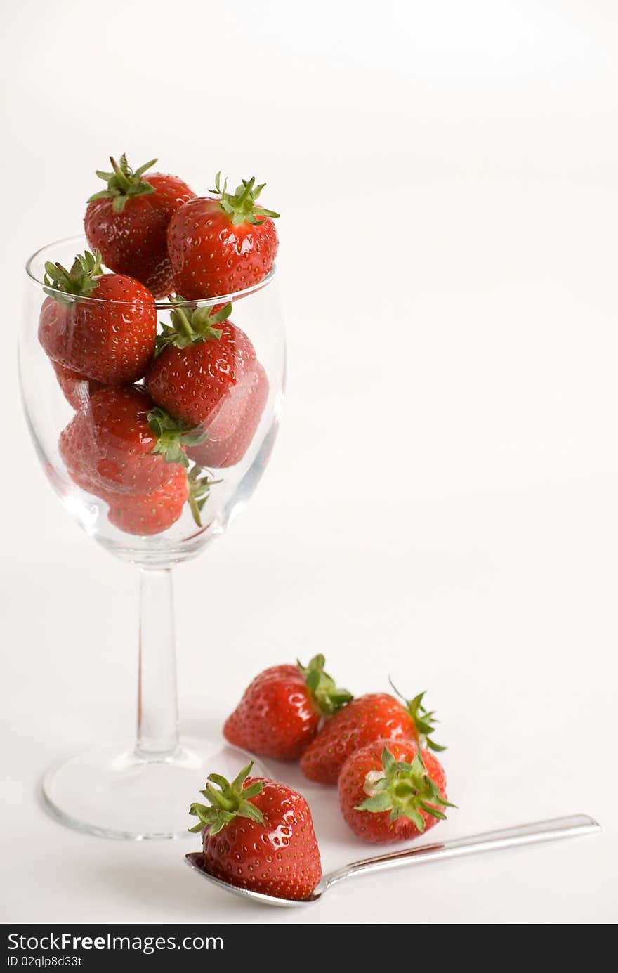 A vertical image of a wine glass filled with fresh strawberries and a spoon with one strawberry on top. A vertical image of a wine glass filled with fresh strawberries and a spoon with one strawberry on top