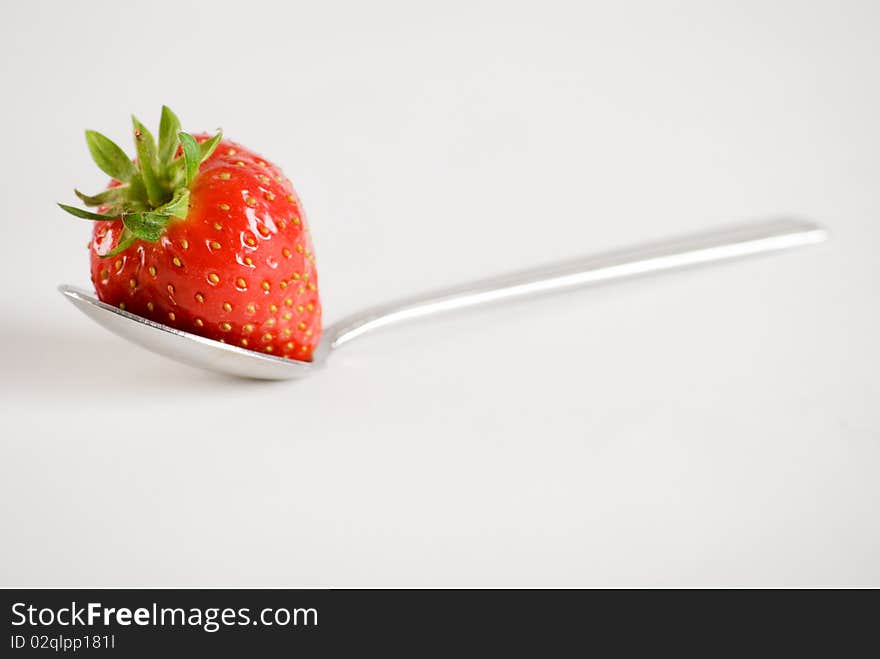 a horizontal image of a fresh strawberry on a spoon. a horizontal image of a fresh strawberry on a spoon