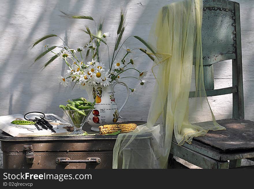 the bouquet of camomiles stands in a jug, alongside book, peas, chair and suitcase. the bouquet of camomiles stands in a jug, alongside book, peas, chair and suitcase