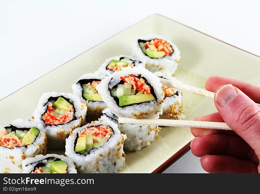 A hand holding a set of chop sticks with sushi. A hand holding a set of chop sticks with sushi.