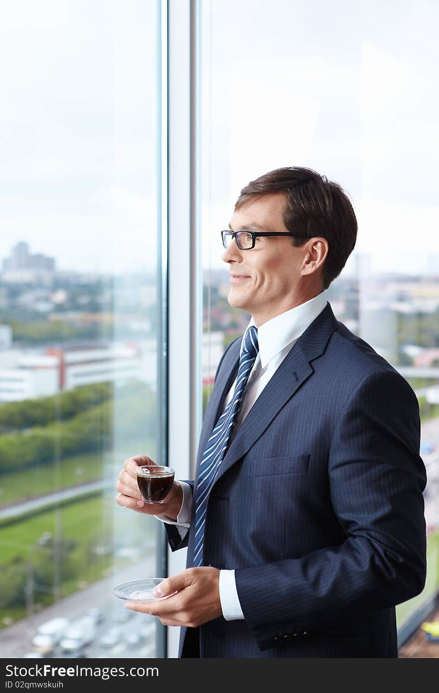 Head of drinking coffee by the window in the office