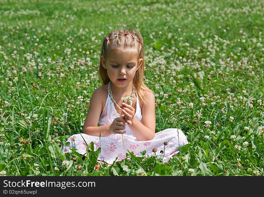 A little girl sitting in the meadow with flowers