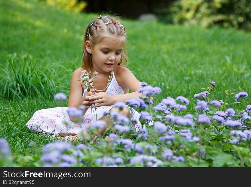 A little girl sitting in the meadow with flowers