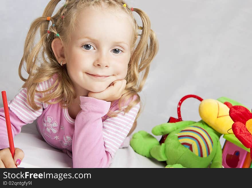 Cute little blond girl with positive facial expression drawing with red pencil and smiling happily. Cute little blond girl with positive facial expression drawing with red pencil and smiling happily