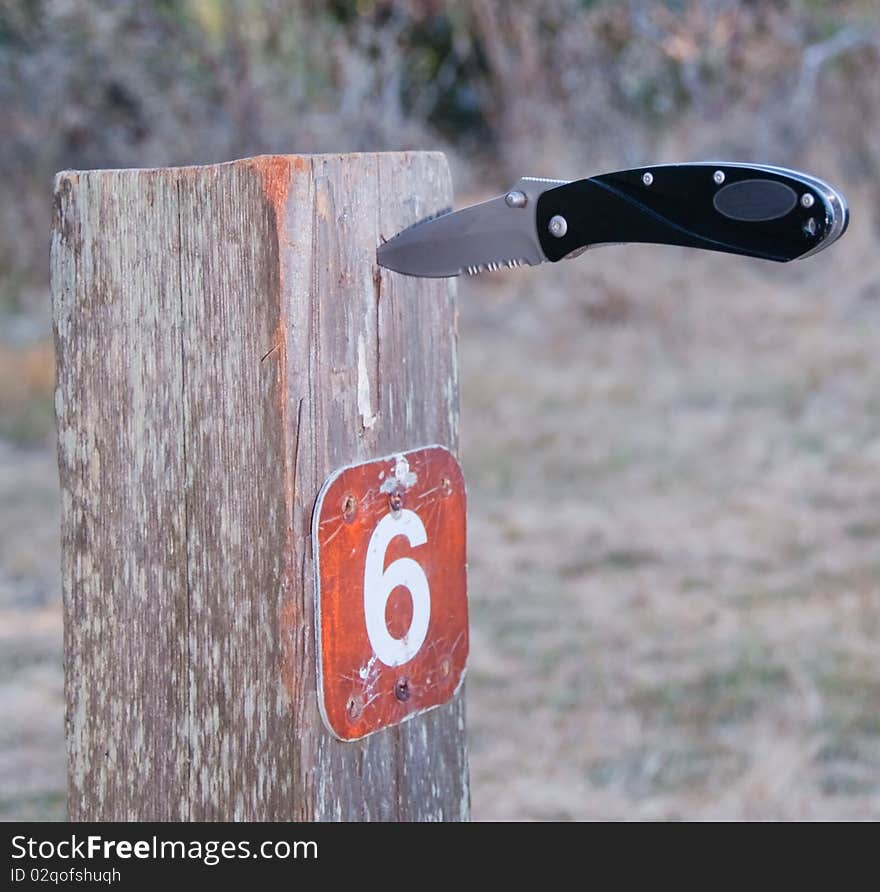 Folding knife stuck in camp site sign post. Folding knife stuck in camp site sign post