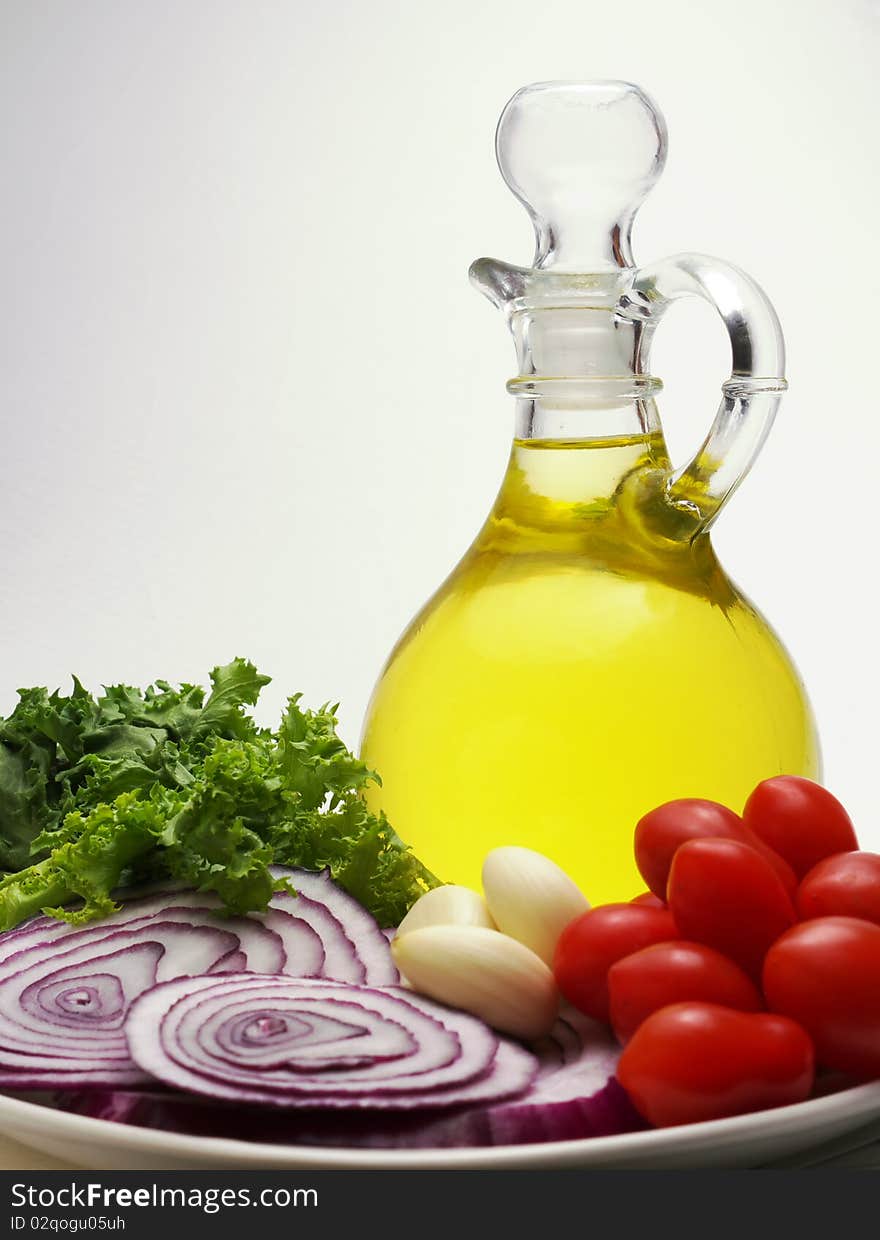 Decanter of olive oil with tomatoes, garlic, sliced red onions, greens, on white background, copyspace. Decanter of olive oil with tomatoes, garlic, sliced red onions, greens, on white background, copyspace