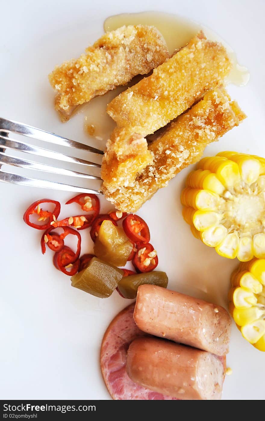 Various food for breakfast, with fork in white dish, corn, sausage, ham, fried meat and some pickle. Various food for breakfast, with fork in white dish, corn, sausage, ham, fried meat and some pickle.