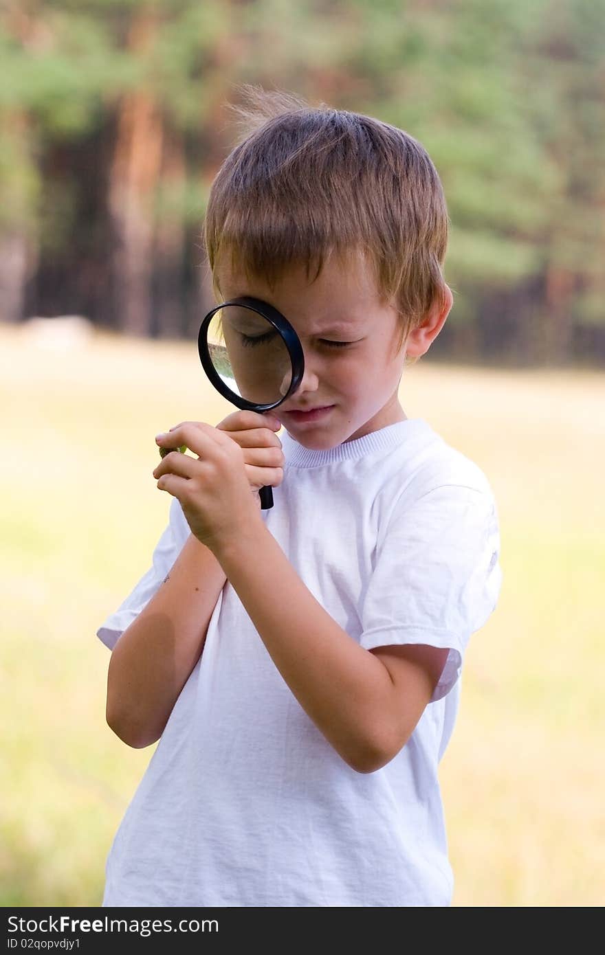 Happy boy with a magnifying glass outdoors on a summer day