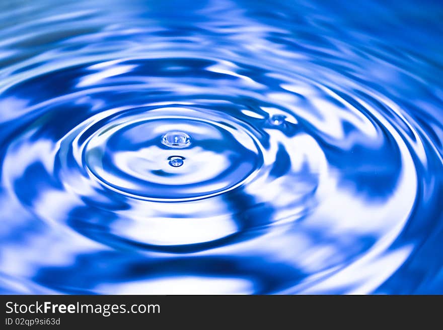 Clean blue drop of water splashing in clear water. Abstract blue background