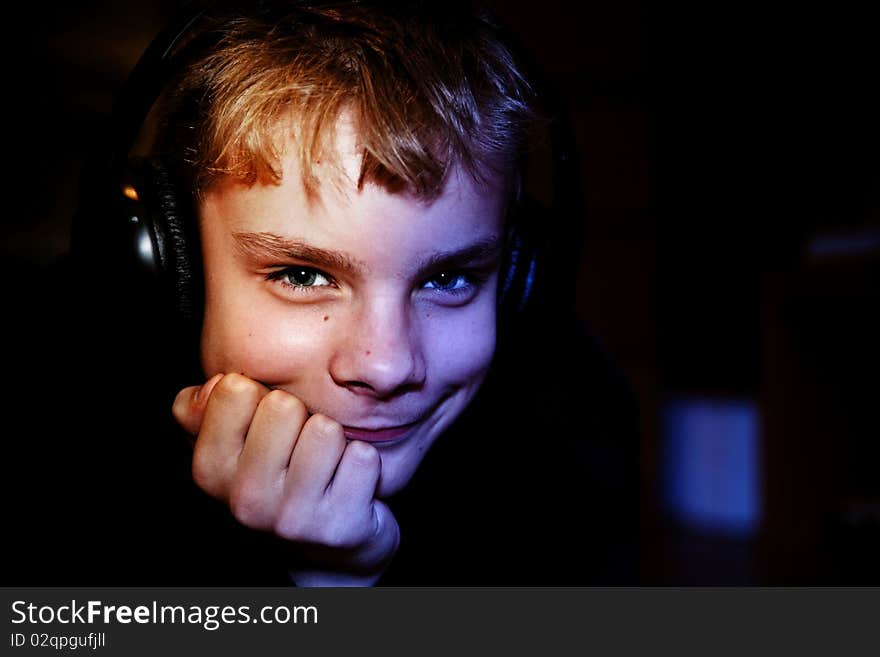 Portrait of the cute teenager with headphones on a dark background close up