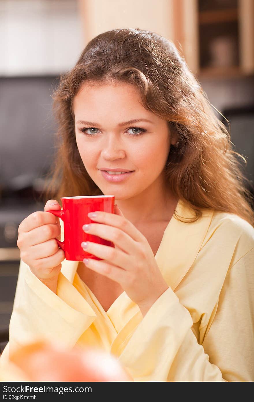 Attractive young adult with red cup of tea in the kitchen. Attractive young adult with red cup of tea in the kitchen