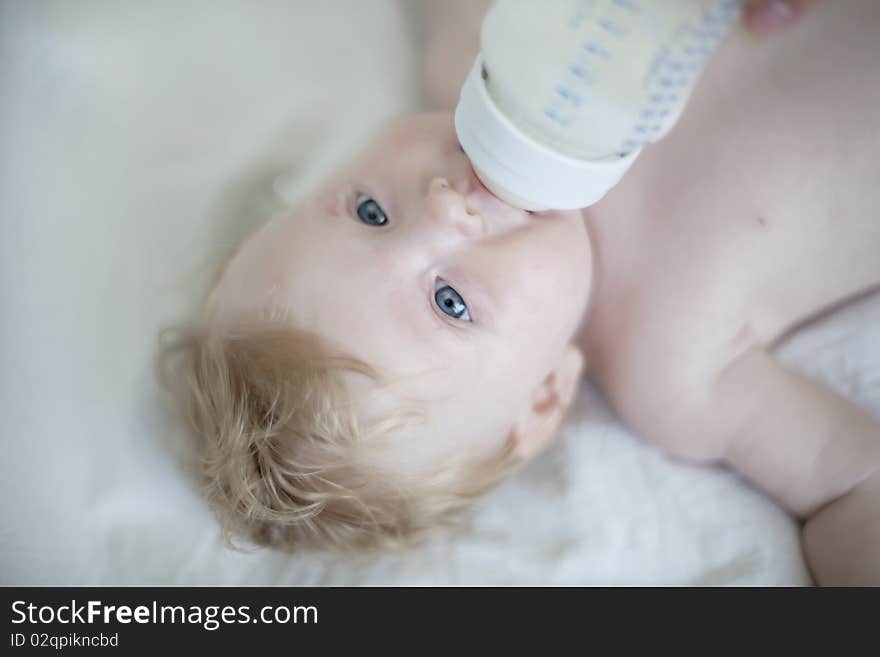 Baby drinking a bottle of milk on the bed