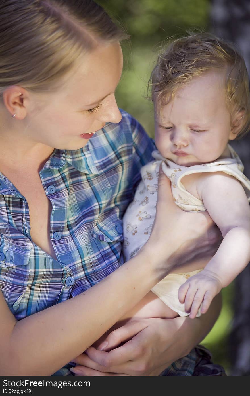 Happy mother holding unhappy baby in the hands - outdoors. Happy mother holding unhappy baby in the hands - outdoors