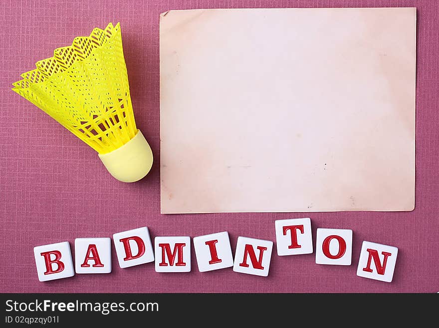 A yellow synthetic badminton shuttlecock next to a piece of paper. Add your text to the paper.