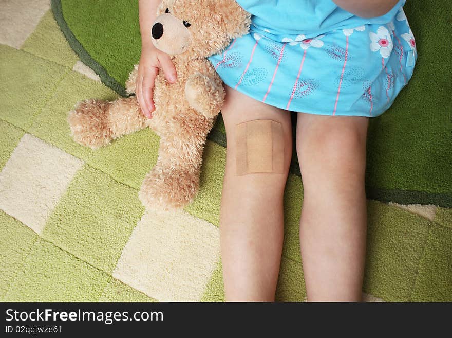 A girl with plaster on knee holiding teddy bear