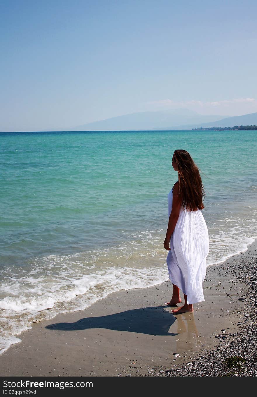 Beautiful woman in white long dress relax on the beach. Greece. Aegean Sea