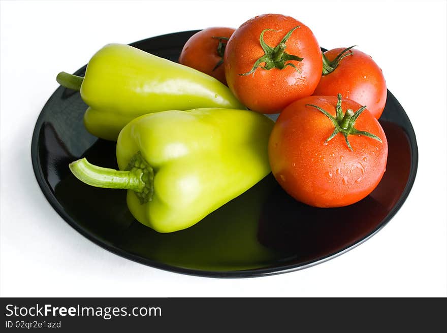 Fresh tomatoes and peppers washed and placed in a black ceramic plate isolated on white background. Fresh tomatoes and peppers washed and placed in a black ceramic plate isolated on white background