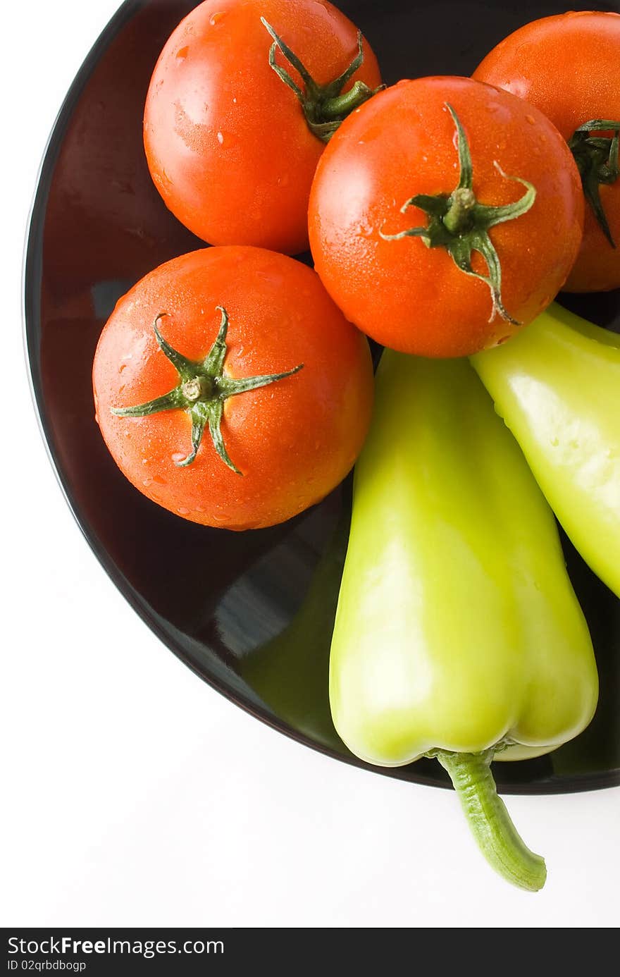 Tomatoes and peppers washed and placed in a black ceramic plate isolated on white background top view