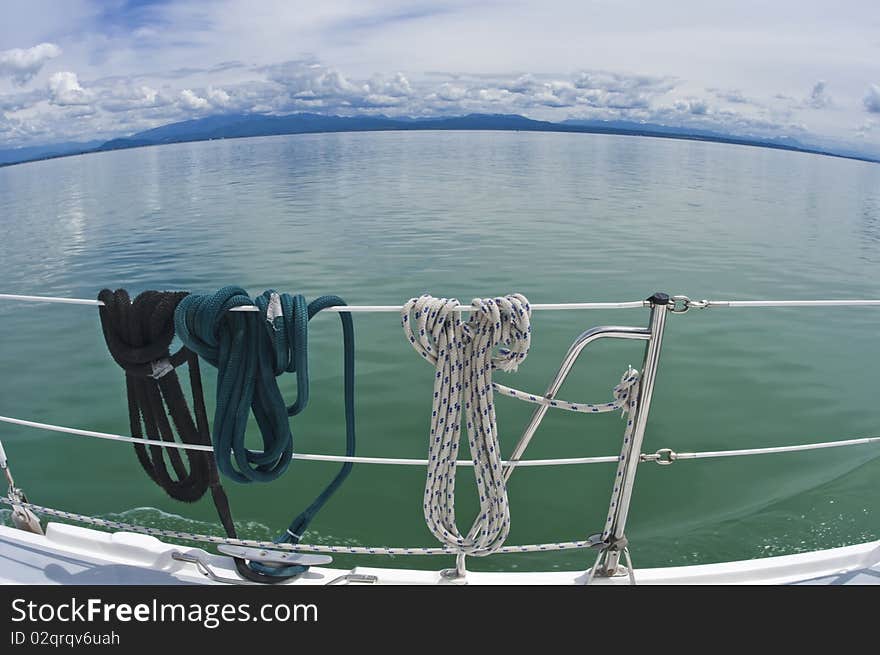 Ropes hanging on the deck of a sailboat and the beautiful view of sea and mountains of Canada from a fish-eye lens. Ropes hanging on the deck of a sailboat and the beautiful view of sea and mountains of Canada from a fish-eye lens.