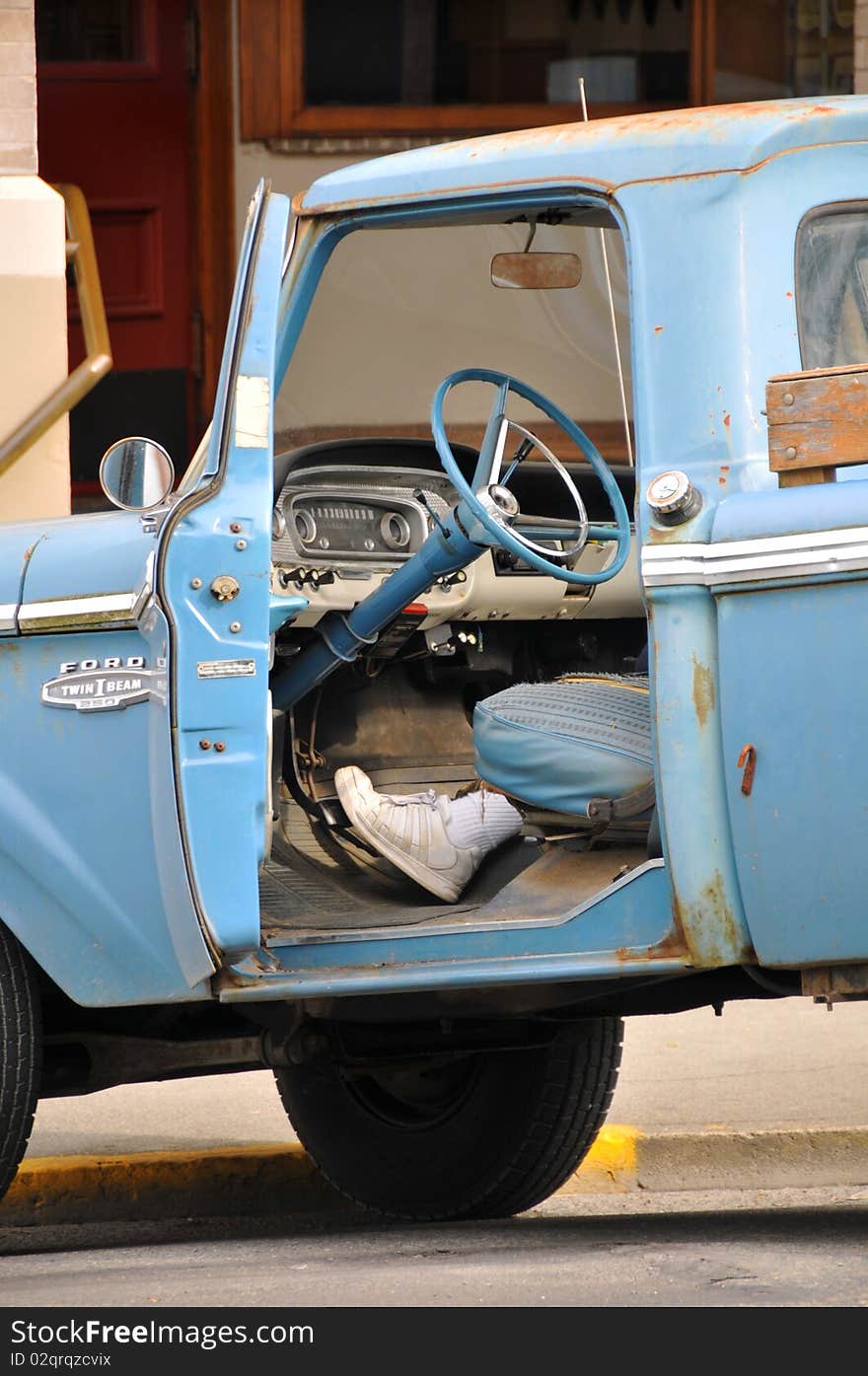 Old blue rusted truck parked by the street, door opened and one foot on the brake pedal. Old blue rusted truck parked by the street, door opened and one foot on the brake pedal.