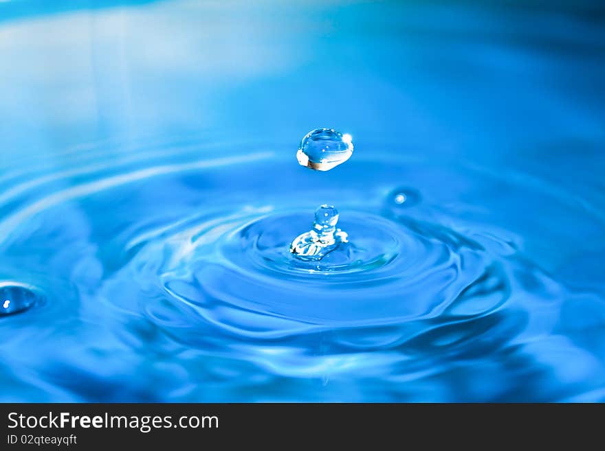 Clean blue drop of water splashing in clear water. Abstract blue background