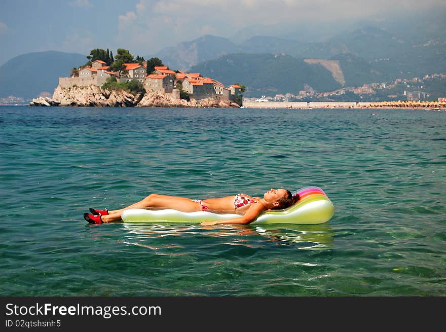 A girl sunbathing on a mattress in Adriatic waters against Sveti Stefan in Montenegro