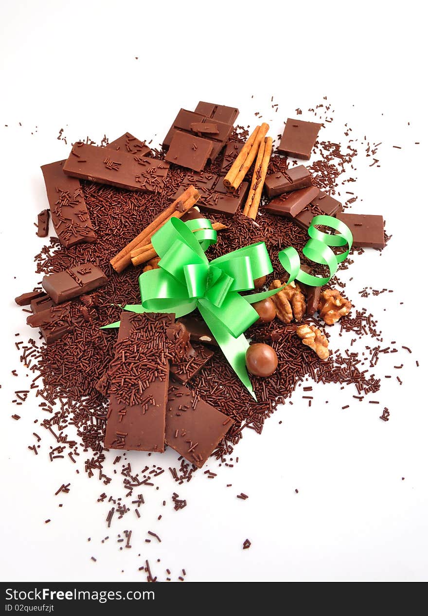 The broken chocolate, chocolate shaving cinnamon and nuts and a green bow on a white background. The broken chocolate, chocolate shaving cinnamon and nuts and a green bow on a white background