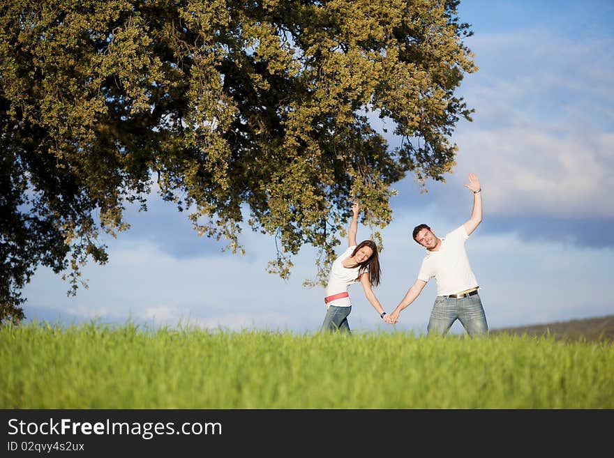 Young beautiful couple hand by hand doing some sport movements under a tree. Young beautiful couple hand by hand doing some sport movements under a tree.