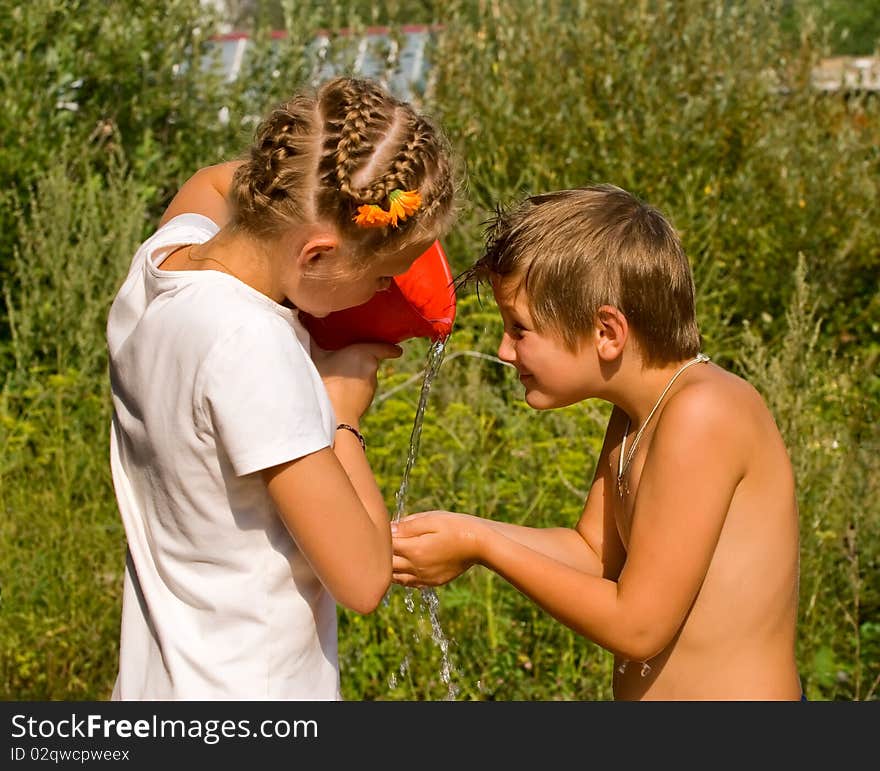 Children wash in the street in summer day from a red bucket. Children wash in the street in summer day from a red bucket