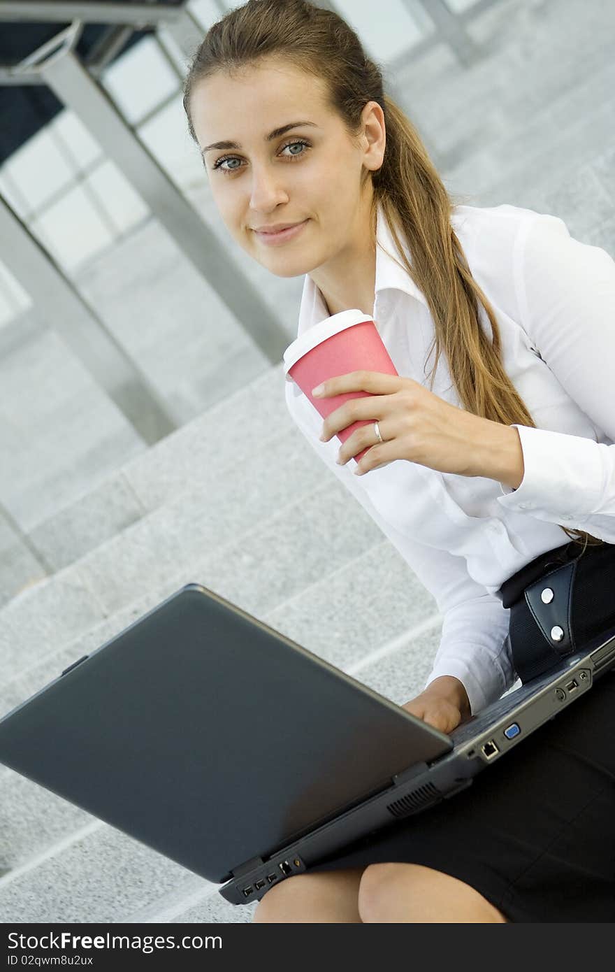 Young, beautiful woman business over coffee in the fresh air sitting on the stairs, office building, next to the laptop. Young, beautiful woman business over coffee in the fresh air sitting on the stairs, office building, next to the laptop.