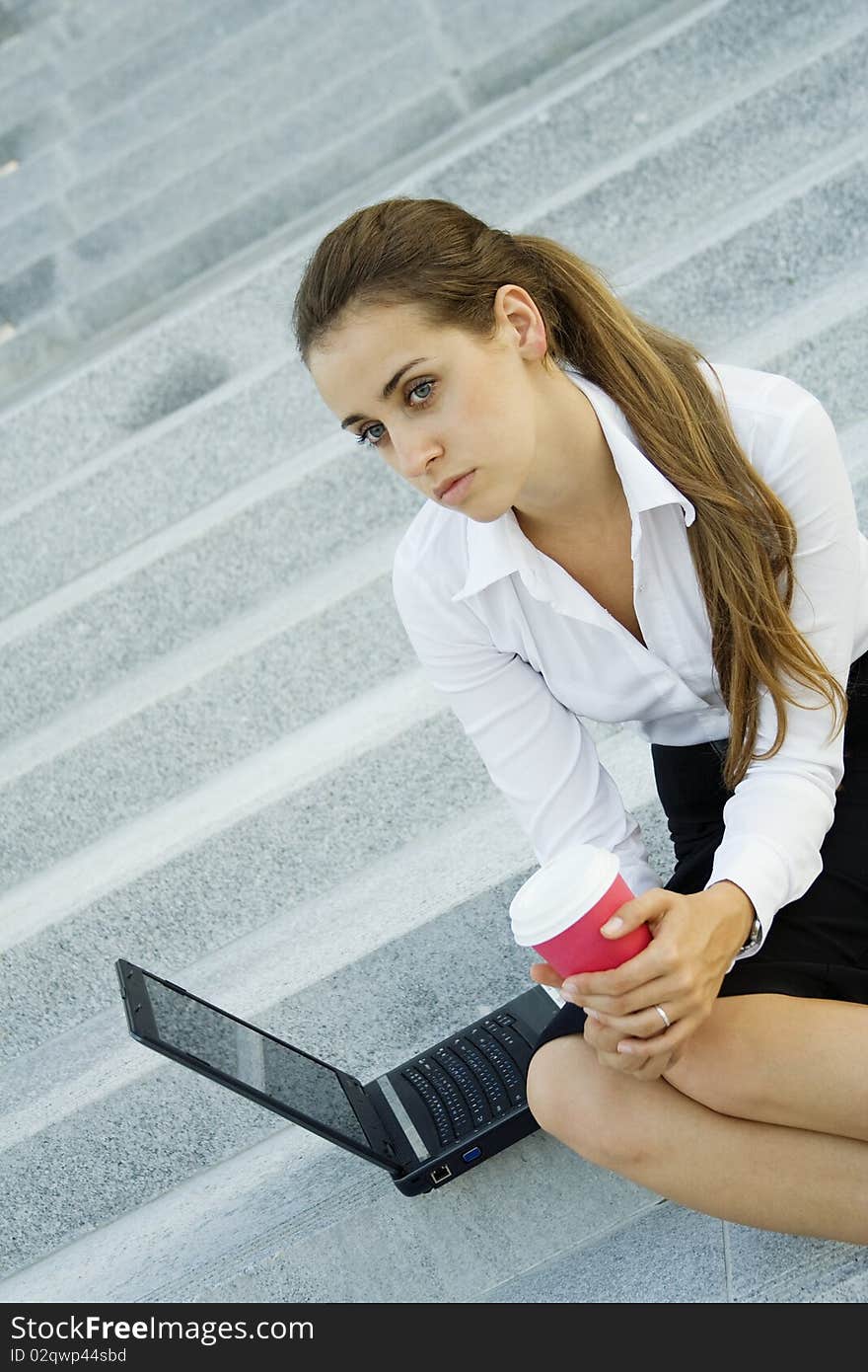 Young, beautiful woman business over coffee in the fresh air sitting on the stairs, office building, next to the laptop. Young, beautiful woman business over coffee in the fresh air sitting on the stairs, office building, next to the laptop.