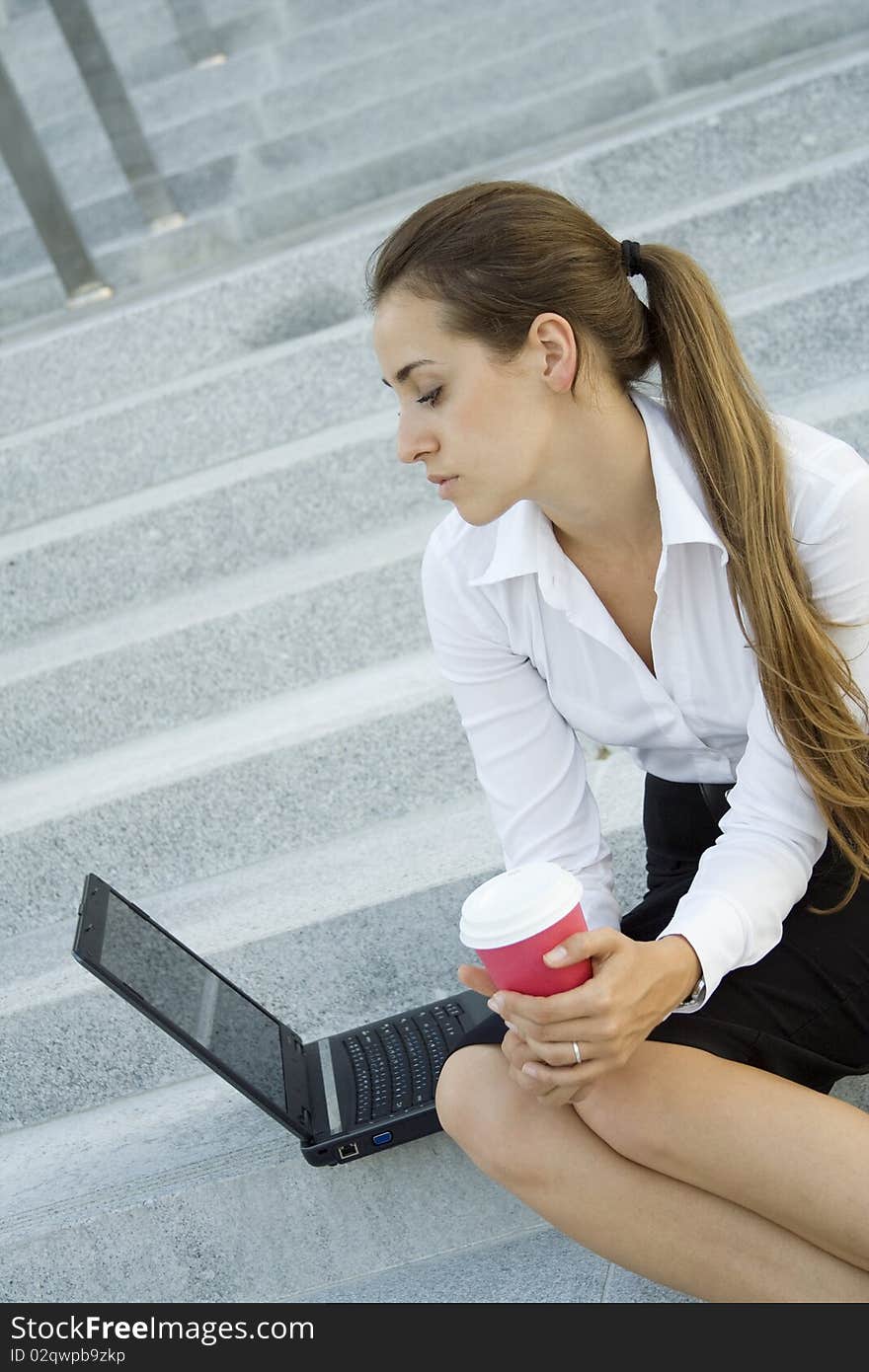 Young, beautiful woman business over coffee in the fresh air sitting on the stairs, office building, next to the laptop. Young, beautiful woman business over coffee in the fresh air sitting on the stairs, office building, next to the laptop.