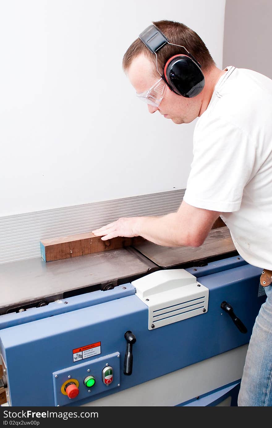 Carpenter working on an electric buzz saw cutting some boards, he is wearing safety glasses and hearing protection to make things safe