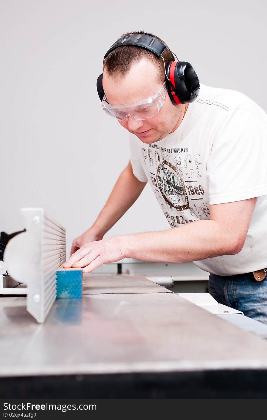 Carpenter working on an electric buzz saw cutting some boards, he is wearing safety glasses and hearing protection to make things safe