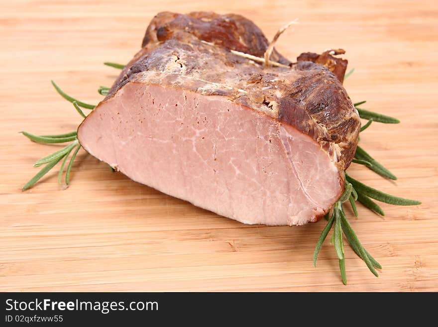 Piece of ham decorated with rosemary on a wooden background