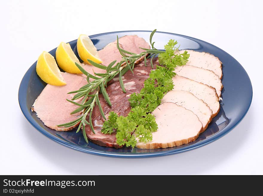 Plate of assorted cold cuts (ham, sirloin, headcheese) decorated with rosemary, parsley and lemon