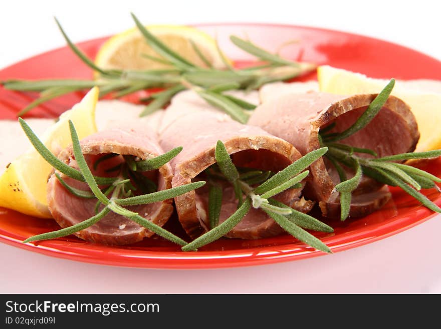 Rolled slices of ham filled with rosemary on a plate decorated with lemon