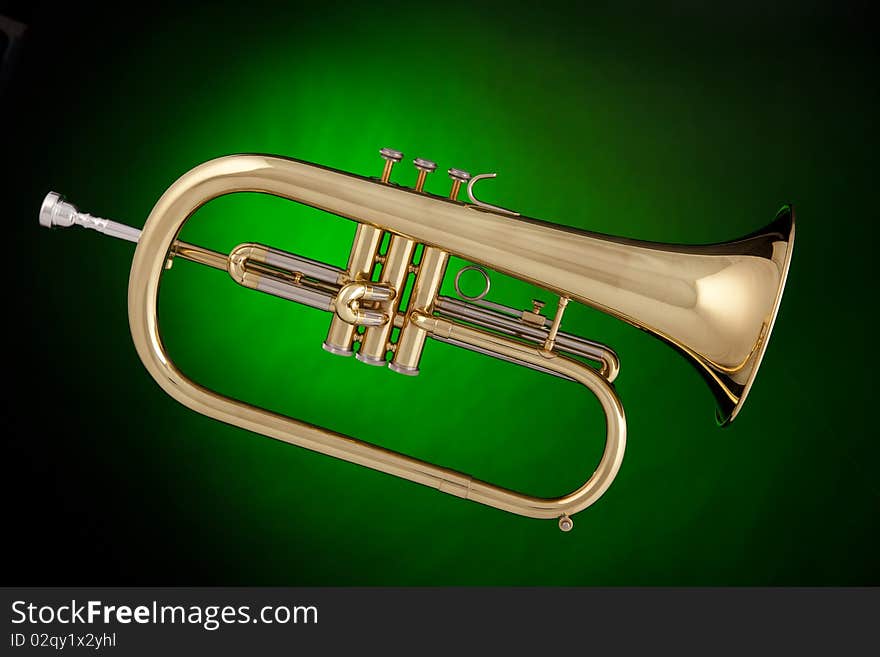 A gold flugalhorn trumpet isolated against a spotlight green background. A gold flugalhorn trumpet isolated against a spotlight green background.