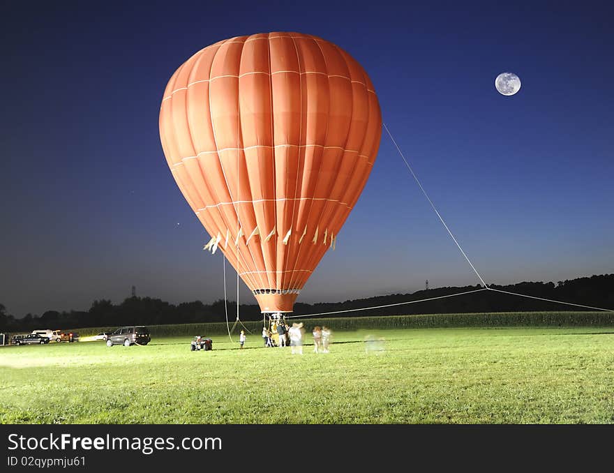 A red hot air balloon photographed at night. Note the full moon, blue sky and green grass. A red hot air balloon photographed at night. Note the full moon, blue sky and green grass