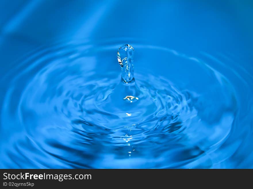 Clean blue drop of water splashing in clear water. Abstract blue background