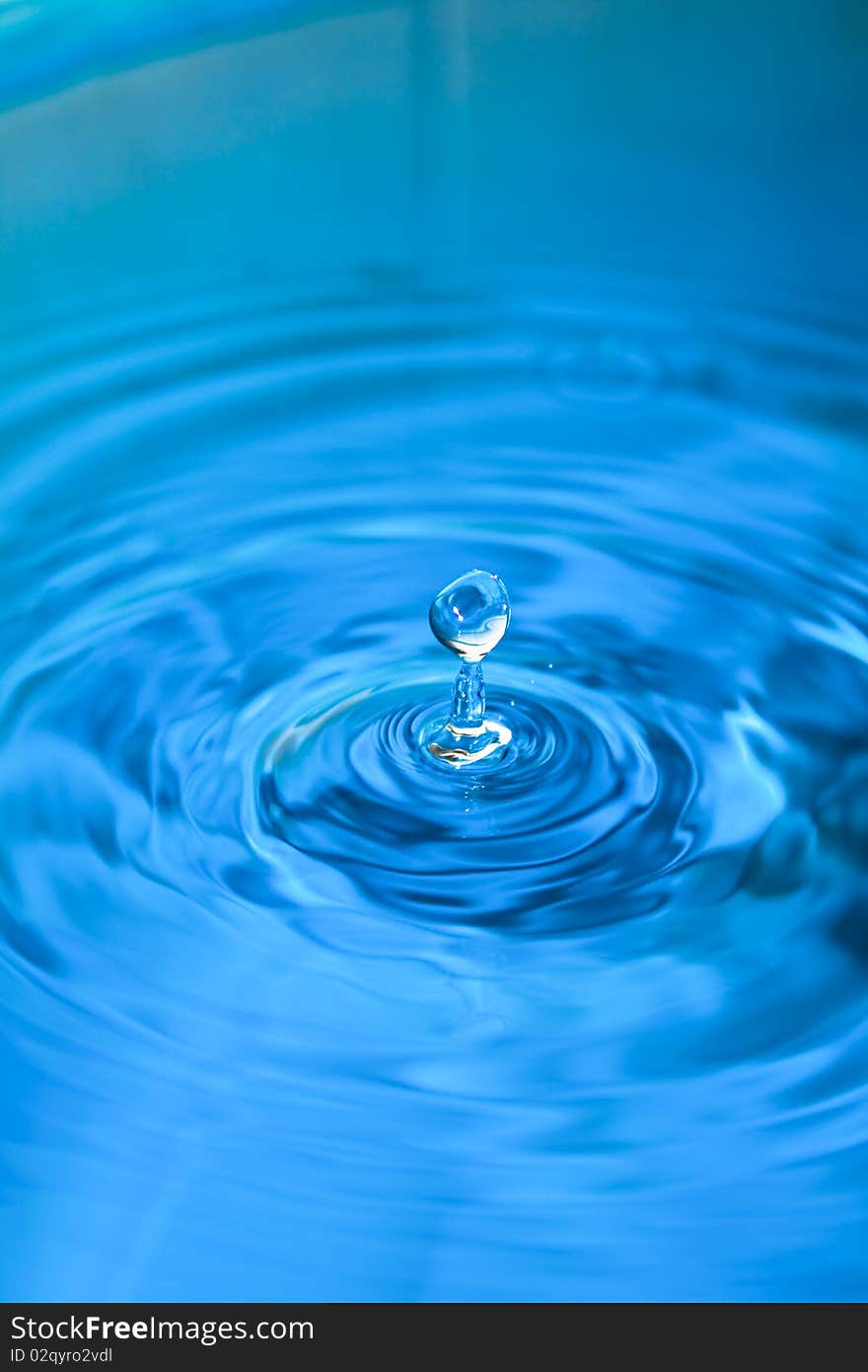 Clean blue drop of water splashing in clear water. Abstract blue background